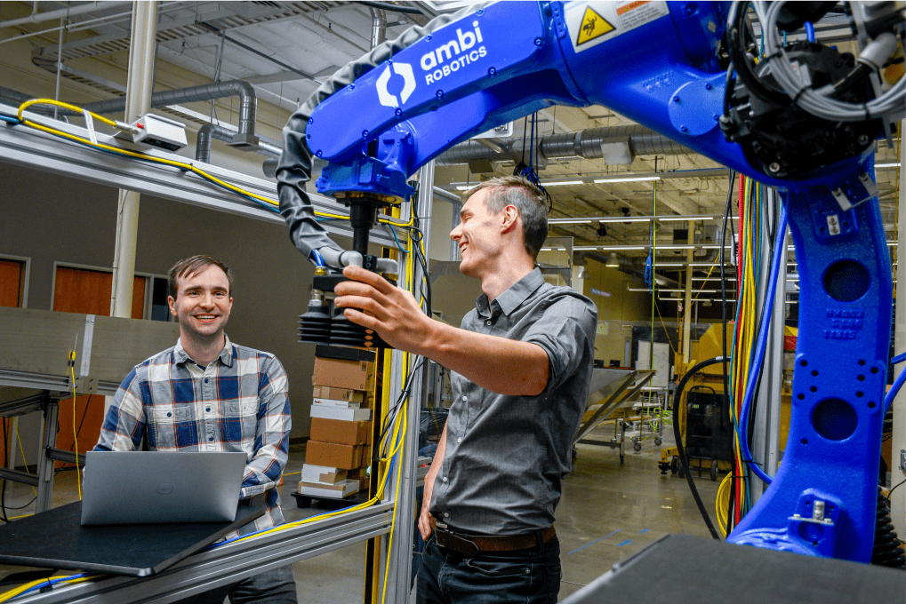 Matt Matl and David Gealy, co-founders of Ambi Robotics, strategize in front of AmbiSort, brainstorming enhancements for our sort-to-sack robotics system.